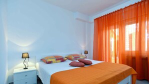 A bedroom with a bed, two bedside tables, a lamp, and orange curtains. - Holiday apartment with air conditioning (Fažana)
