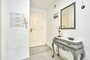 A hallway with a white door, a telephone, a mirror, and a marble-topped console table.