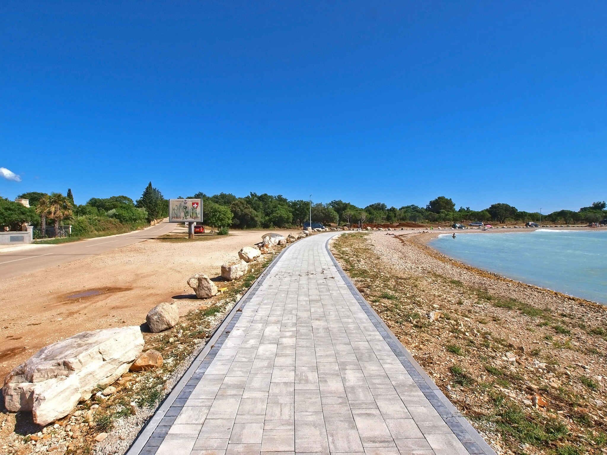 A paved walkway along a beach with a clear blue sky.