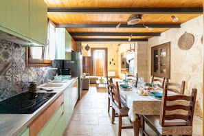Une cuisine avec des meubles en bois, une table à manger avec des chaises et un mur en pierre.
