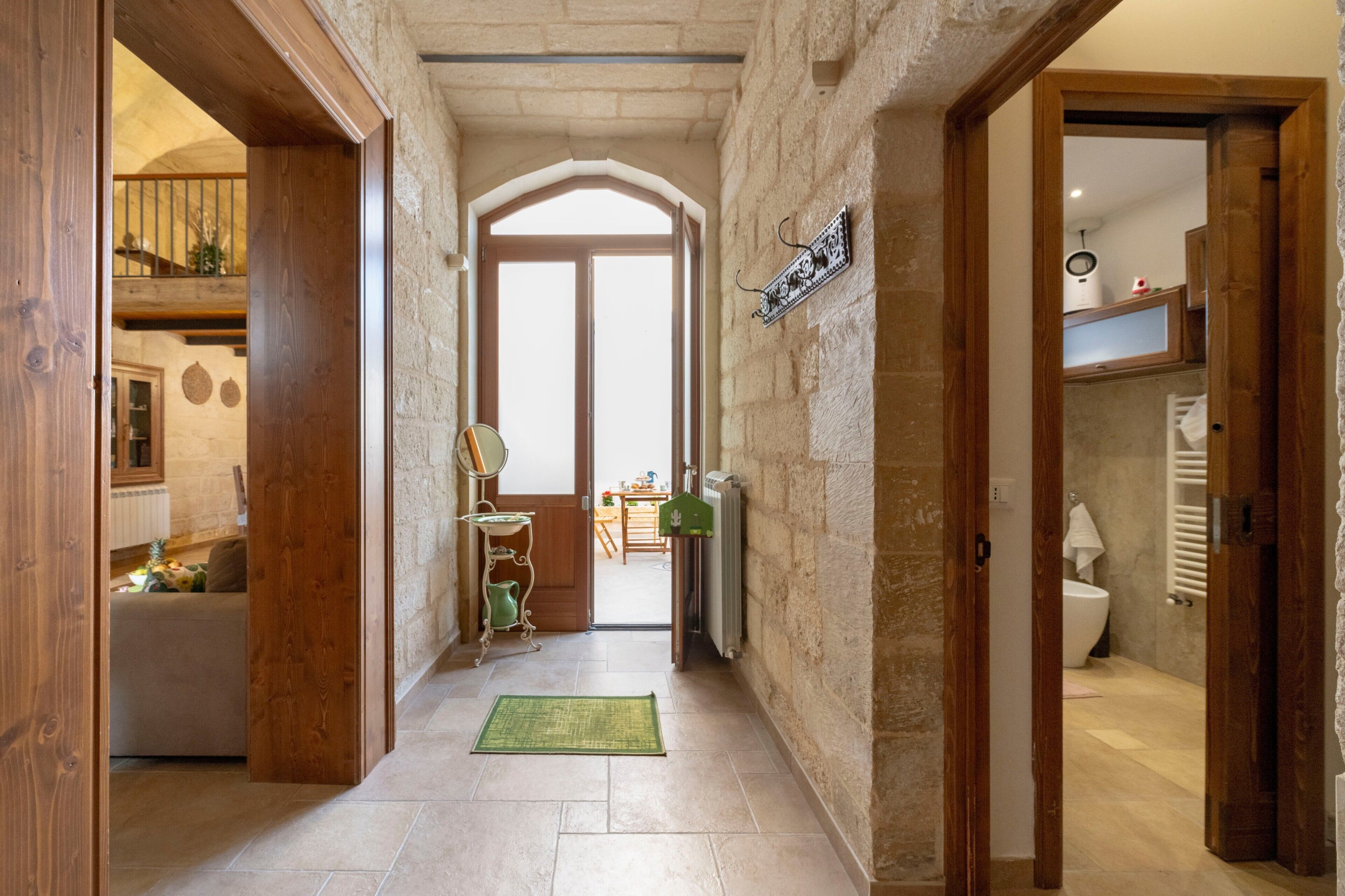 Un pasillo estrecho con paredes de piedra, puertas de madera y vista a una habitación con cama y mesa.