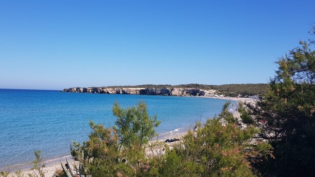 Et kystlandskab med klart blå hav, klippefremspring og en sandstrand.