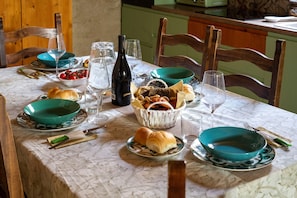 Une table à manger dressée avec des bols verts, des verres à vin, une bouteille et du pain.