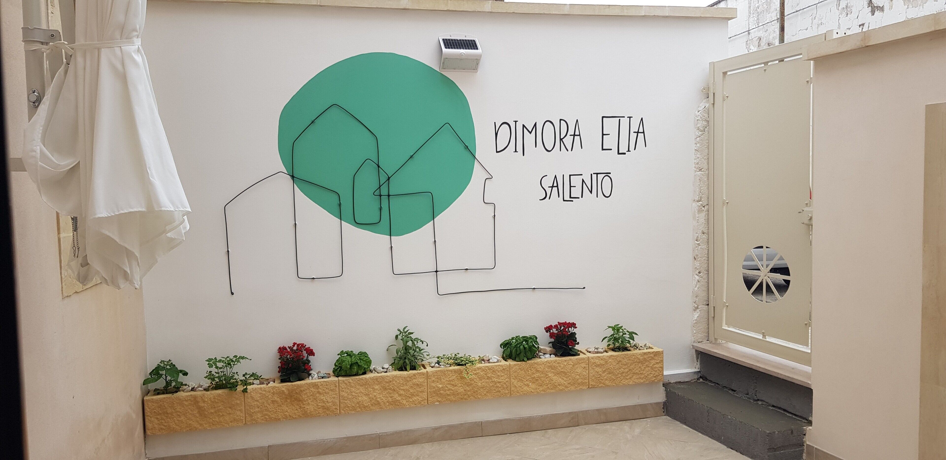 A wall with a geometric design, a nameplate, and a planter with plants.
