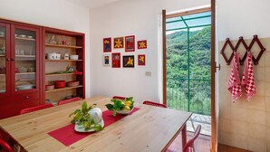 Een eethoek met een houten tafel, rode stoelen, een rode kast met glazen deuren en een balkon met een groene balustrade.