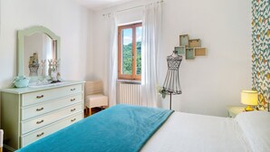 Een slaapkamer met een bed, een dressoir, een spiegel, een raam en decoraties aan de muur.