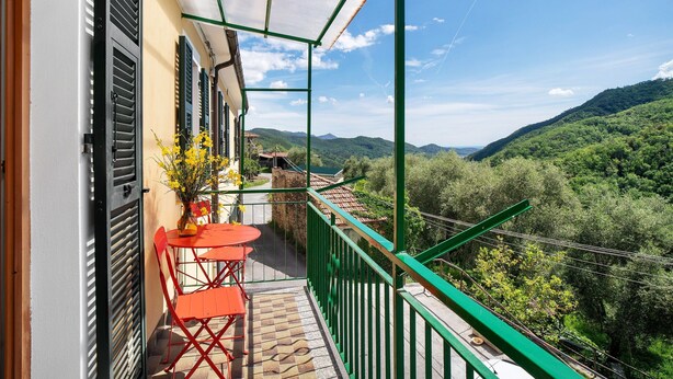 Een balkon met uitzicht op een groene vallei, een betegelde vloer en een tafel met stoelen.