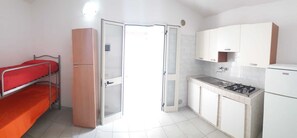 Een compacte kamer met een stapelbed, een kitchenette met een kookplaat en gootsteen, en een deur naar een andere kamer.