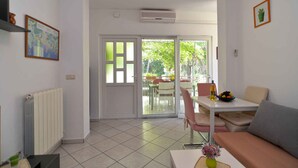 Una sala de estar con un sofá, una mesa con un frutero, una silla, un radiador, un mapa en la pared y un ventanal corredero que da a un área exterior.