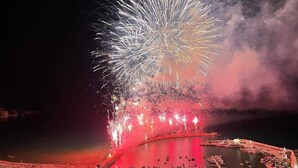 A fireworks display over a waterfront area with boats and a large open space.