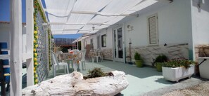 Un espacio al aire libre cubierto con una mesa, sillas, plantas en macetas y un adorno blanco.