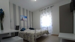 A bedroom with a bed, a desk, a chair, a TV, and a painting on the wall.