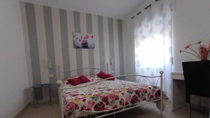A single-bed room with a striped wall, a small bedside table, a desk with a chair, and a window with curtains. - Apartment 'Deluxe Room' with Private Terrace, Wi-Fi and Air Conditioning (Valle Clavia)