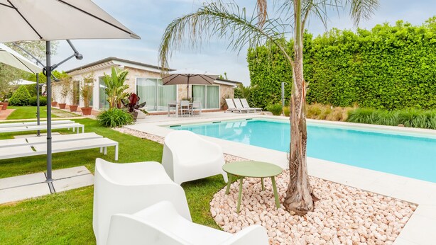 Un espace piscine aménagé avec des chaises longues, une table et un palmier.