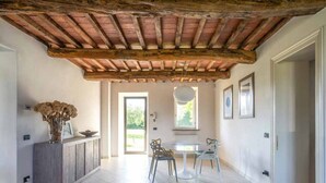 Un hall spacieux avec un plafond en bois rustique, un coin repas avec une table et des chaises, et une vue sur un espace extérieur, accessible par une porte.