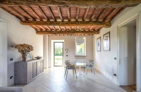 A spacious hallway with a rustic wooden ceiling, a dining area with a table and chairs, and a view through a doorway to an outdoor space.