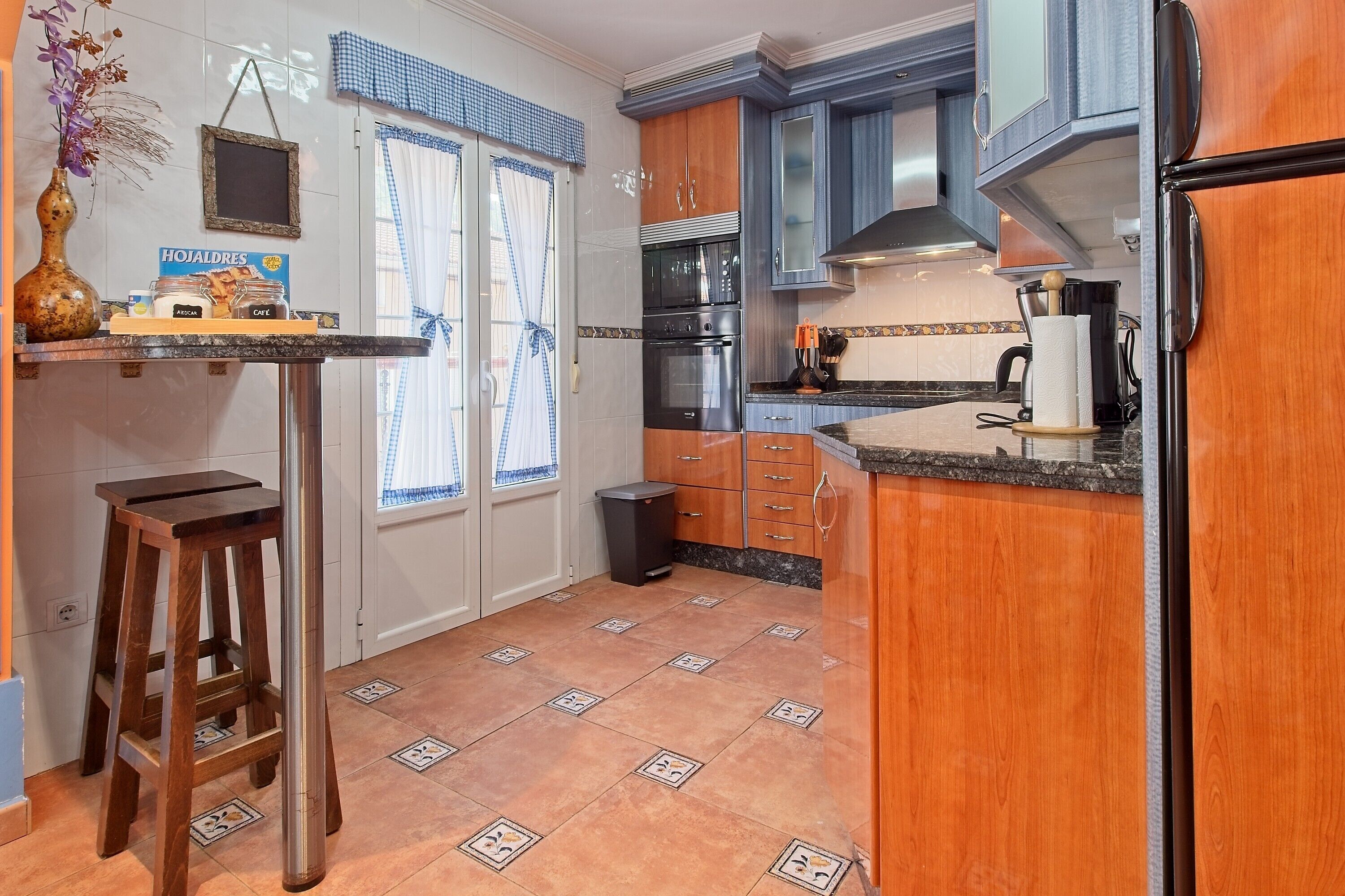Una cocina con armarios de madera, una estufa negra, un fregadero y un taburete pequeño.