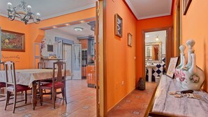 A dining area with a table and chairs, a hallway with a mirror, and a kitchen in the background.
