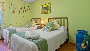 A room with two beds, a nightstand, a lamp, a wall art piece, and a large blue container.