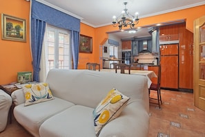 A living room with a sofa, a dining table, and a kitchen in the background.