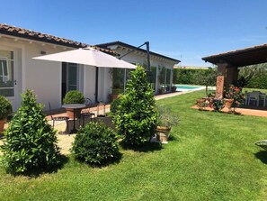 Een verzorgd terras met tuinmeubilair, een zwembad en een tuin met vormgesnoeide struiken.