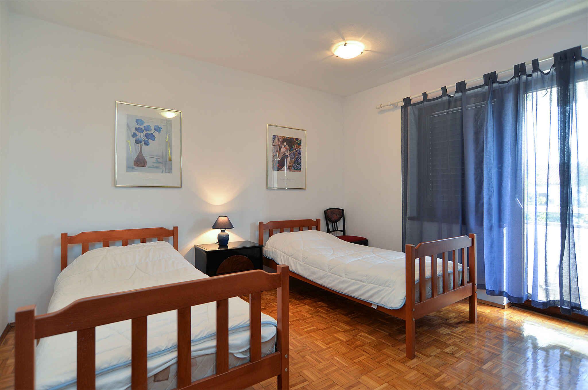 Ein Zimmer mit zwei hölzernen Betten, einem Nachttisch mit Lampe und einem Sessel. An der Wand hängen zwei gerahmte Bilder.