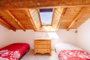 A room with a sloped wooden ceiling, a skylight, two beds with patterned bedding, and a wooden nightstand.