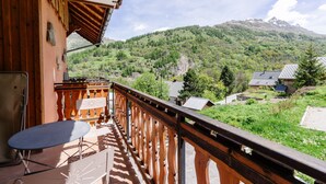 Un balcón con mesa y sillas, con vistas a un paisaje montañoso y una casa al fondo.