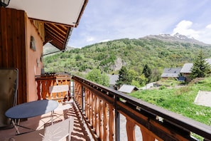 A balcony with a table and chairs, overlooking a mountainous landscape with a house in the background.