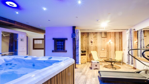 Ein Zimmer mit Whirlpool, Fitnessgeräten, Holzwänden und einem kleinen Tisch mit Stuhl.