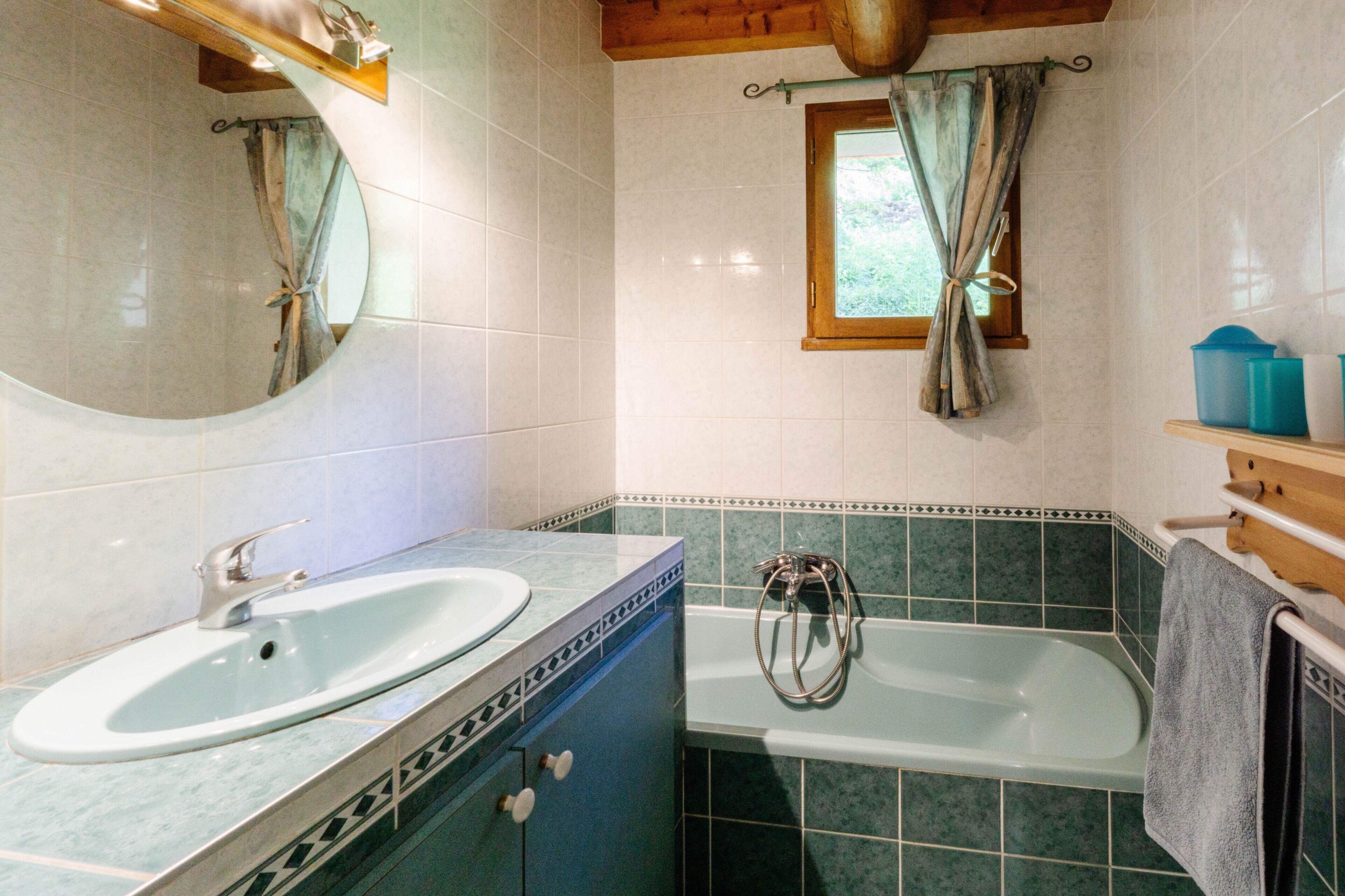 A bathroom with a sink, bathtub, and a window with curtains.