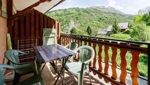 Ein Balkon mit Tisch und Stühlen, der auf eine Berglandschaft blickt.