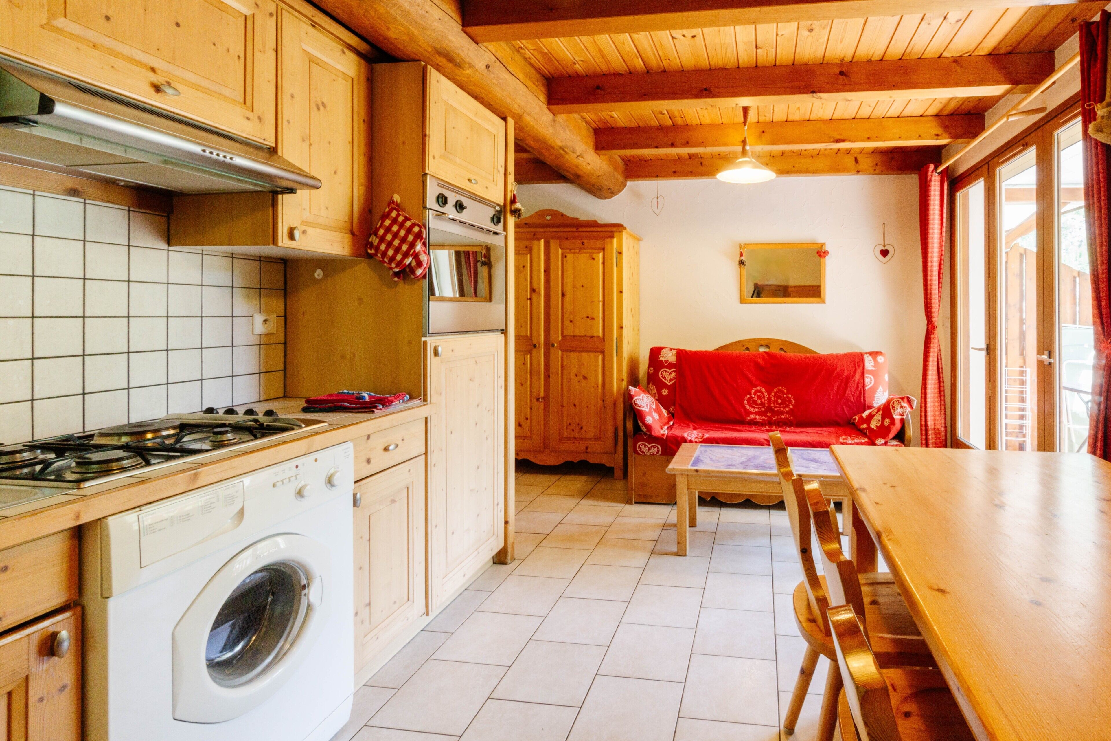A kitchen with wooden cabinets, a stove, a washing machine, and a dining area with a table and chairs.