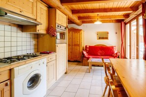 A kitchen with wooden cabinets, a stove, a washing machine, and a dining area with a table and chairs.