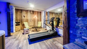 Ein Raum mit Laufband, Massagesessel, kleinem Tisch und Holzwänden.