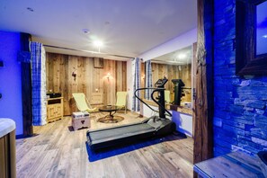 Una habitación con cinta de correr, sillón de masajes, una mesita y paredes de madera.