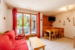 Una habitación con una mesa de comedor de madera, sillas, un banco de madera, un sofá rojo y un ventanal corredero que da a un espacio exterior.