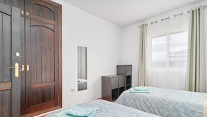 A hotel room with two beds, a wardrobe, a desk, and a window with curtains.