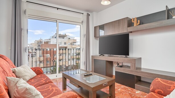 A modern living room with a sofa, a coffee table, a TV, and a balcony with a view of buildings.