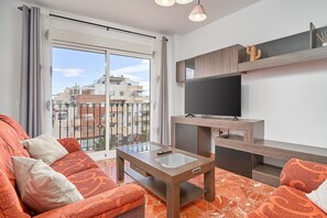 A modern living room with a sofa, a coffee table, a TV, and a balcony with a view of buildings.