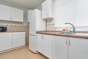 A kitchen with white cabinets, a microwave, a refrigerator, a granite countertop, and a sink with a faucet.