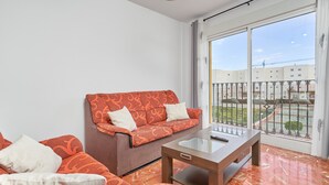 A living room with a sofa, a coffee table, and a large window with a view of buildings and a fence.