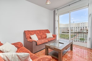 A living room with a sofa, a coffee table, and a large window with a view of buildings and a fence.