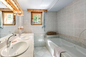 A bathroom with two sinks, a bathtub, and a window with curtains.