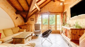 Un interior acogedor de madera con un sofá, una silla, una mesa y un balcón con plantas.