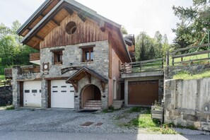 A two-story stone building with a wooden balcony, a stone archway entrance, and two garage doors.