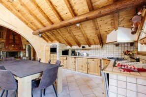 A rustic kitchen with wooden beams, a dining table with chairs, and a tiled backsplash.