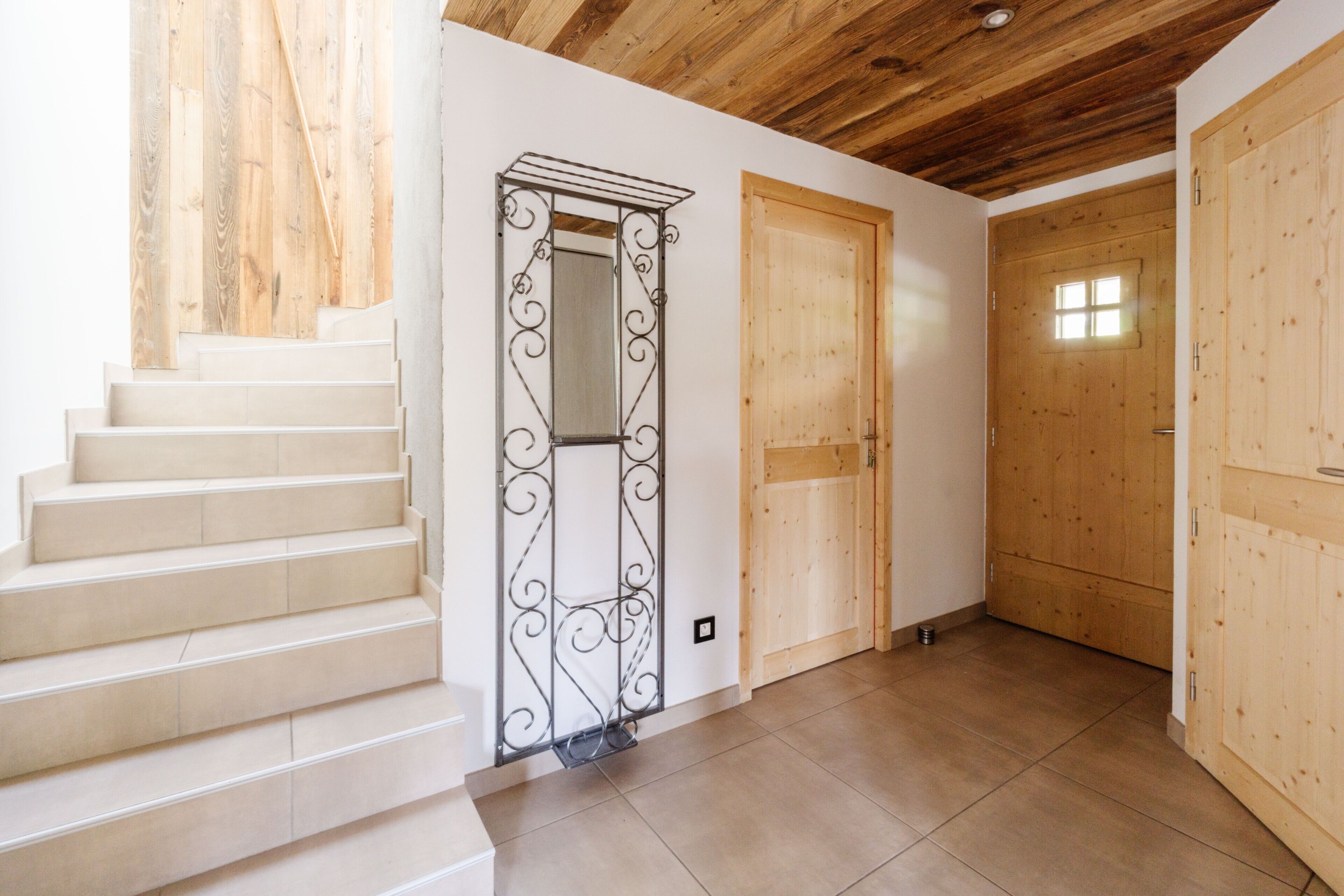 A staircase leading to a wooden door with a small window, a metal decorative element, and a tiled floor.