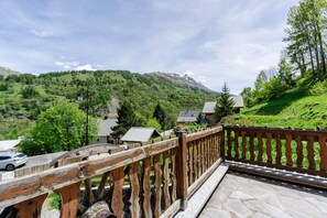 En træterrasse med flisebelægning, der ud til et grønt landskab med træer og et bjerg.
