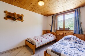 Une chambre à coucher avec deux lits en bois, une tête de lit en bois, une fenêtre avec des rideaux et une étagère en bois ornée de quelques objets décoratifs.
